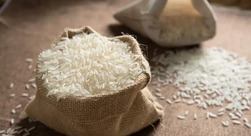 Un sac en toile de jute déborde de riz blanc, une céréale essentielle. Une autre bourse de riz est visible en arrière-plan.