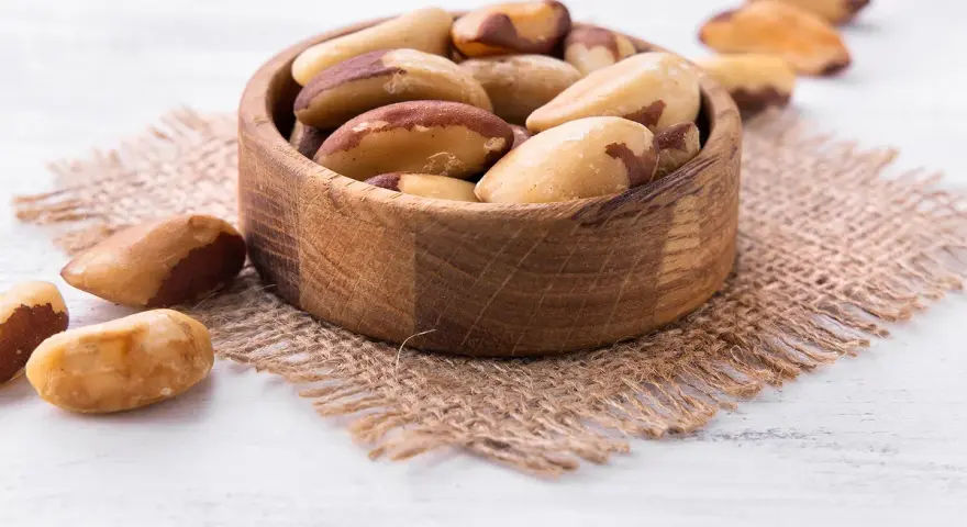 Un bol en bois rempli de noix du Brésil, mettant en avant leurs bienfaits nutritionnels. Quelques noix sont dispersées autour.