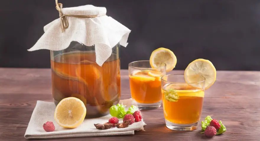 Bocal de kombucha et deux verres garnis de citron, framboises et menthe. Découvrez les kombucha bienfaits pour une boisson rafraîchissante et saine.