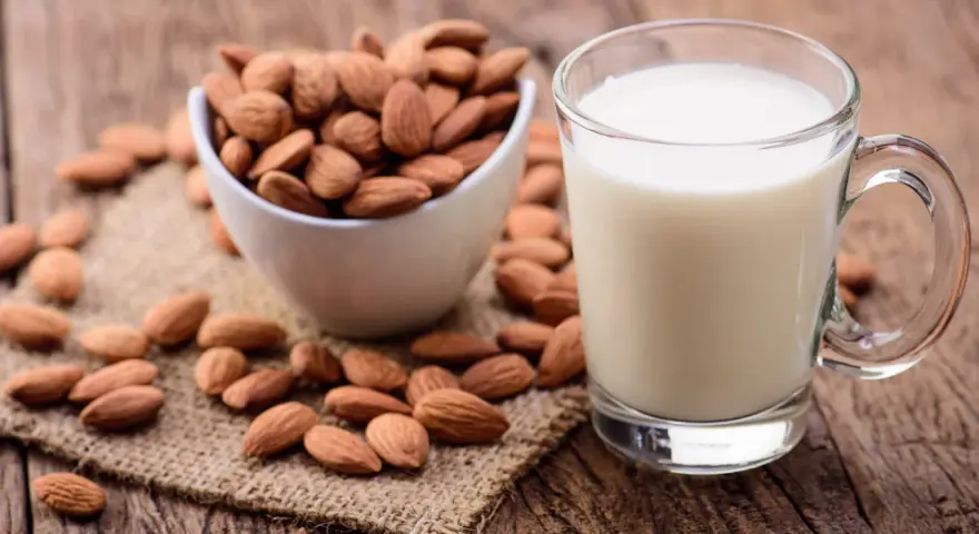 Un verre de lait d'amande frais à côté d'un bol d'amandes entières sur une surface en bois rustique.