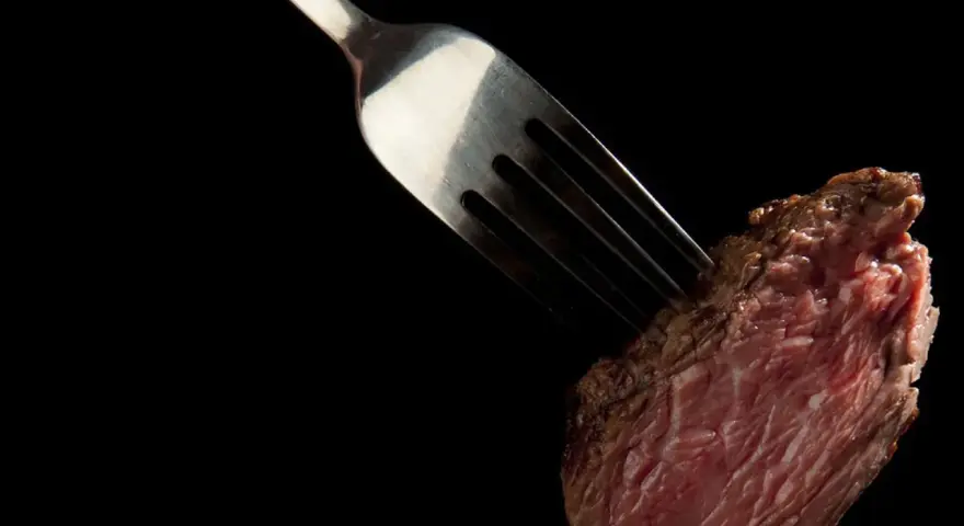 Une fourchette transperce un morceau de viande rouge, rappelant la prudence pour ceux qui ont une allergie au porc.