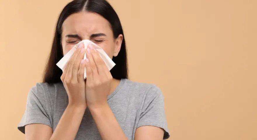 Une jeune femme se mouche dans un mouchoir en papier, le nez bouché par un rhume.
