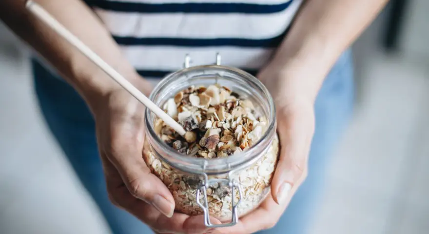 Mains de personne tenant un bocal en verre rempli de muesli maison, avec une cuillère en bois.