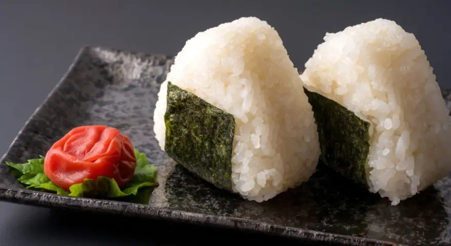 Deux onigiri algue sur une assiette avec une prune salée.