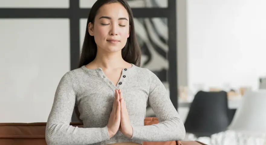 Jeune femme méditant, mains jointes, pour apprendre comment reduire le stress naturellement.