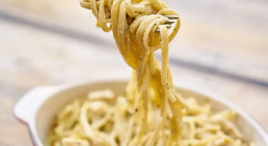 Une fourchette soulève des pâtes crémeuses, peut-être des pâtes cacahuète, d'un plat.