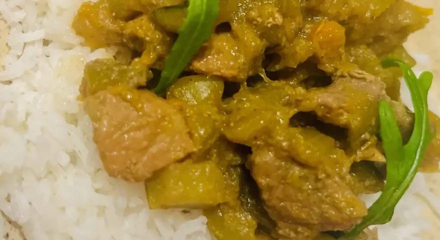 Un plat de riz blanc garni d'un curry vert aux légumes et morceaux de viande.
