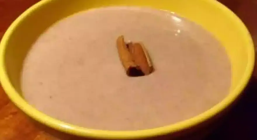 Un bol jaune contient une crème onctueuse de banane au lait de coco, garnie d'un bâton de cannelle.