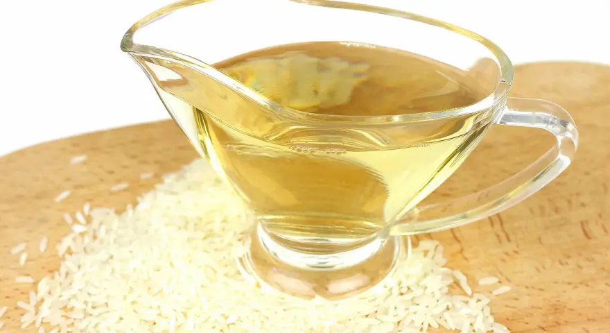 Un vinaigrier en verre rempli de liquide doré, entouré de grains de riz. Une idée pour par quoi remplacer le vinaigre de riz.