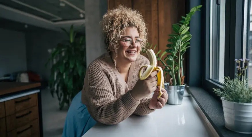 Une femme souriante avec des cheveux bouclés tient une banane, malgré une possible allergie à la banane.