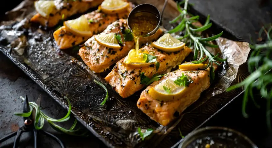 Filets de saumon sauce soja sucrée, garnis de citron et de persil, sur un plateau orné. Une louche verse la sauce.