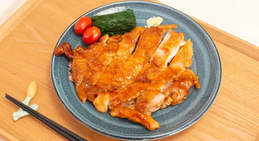 Délicieux poulet teriyaki recette, tranché et glacé, servi avec des tomates cerises et des épinards sur une assiette bleue.