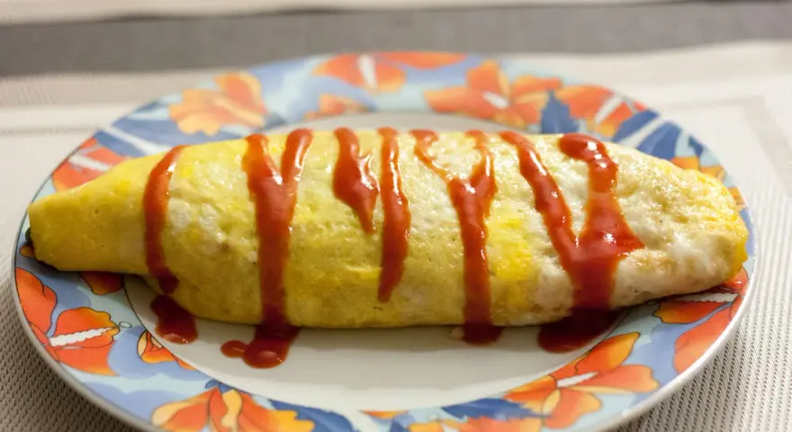 Une omelette japonaise au riz, nappée de ketchup, sur une assiette décorée de fleurs.