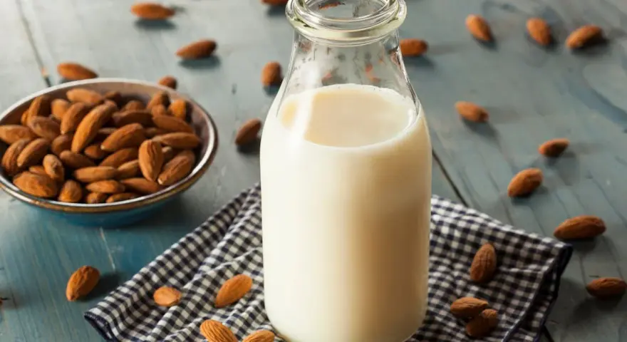 Bouteille de lait végétal d'amande, avec un bol d'amandes et des amandes éparpillées sur une table en bois bleu.