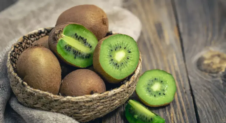 Un panier de kiwis frais, certains entiers, d'autres coupés, révélant leur chair verte et leurs pépins noirs. Attention, le kiwi peut provoquer une allergie.