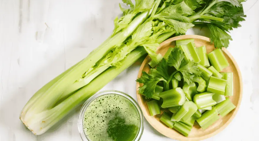 Jus de céleri frais, coupé en morceaux dans un bol en bois. Une branche entière de céleri est à côté. Attention à l'allergie céleri.