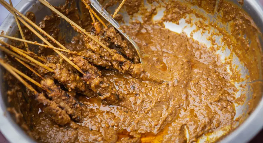 Brochettes de poulet baignant dans une généreuse sauce satay crémeuse, prêtes à être dégustées.