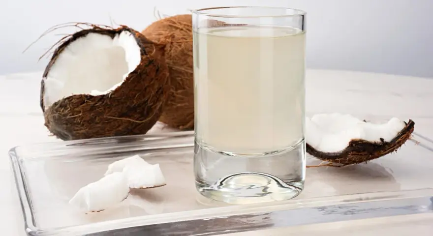Un verre d'eau de coco, entouré de morceaux de noix de coco fraîches. Découvrez les nombreux bienfaits de l'eau de coco pour votre santé.