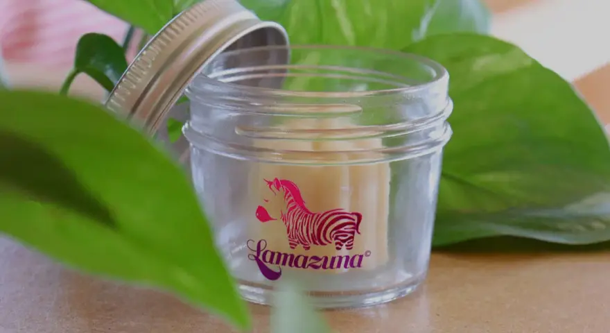 Petit pot en verre ouvert, révélant un baume solide. Le logo Lamazuna, un zèbre rose, orne le verre. Un soin naturel à base de beurre de cacao.
