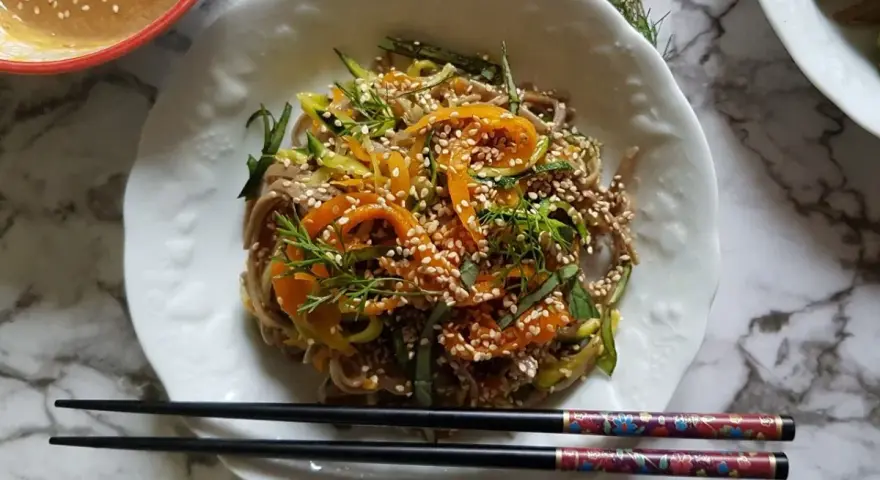 Salade de nouilles soba colorée avec des carottes, des courgettes et des graines de sésame, servie avec une sauce crémeuse.