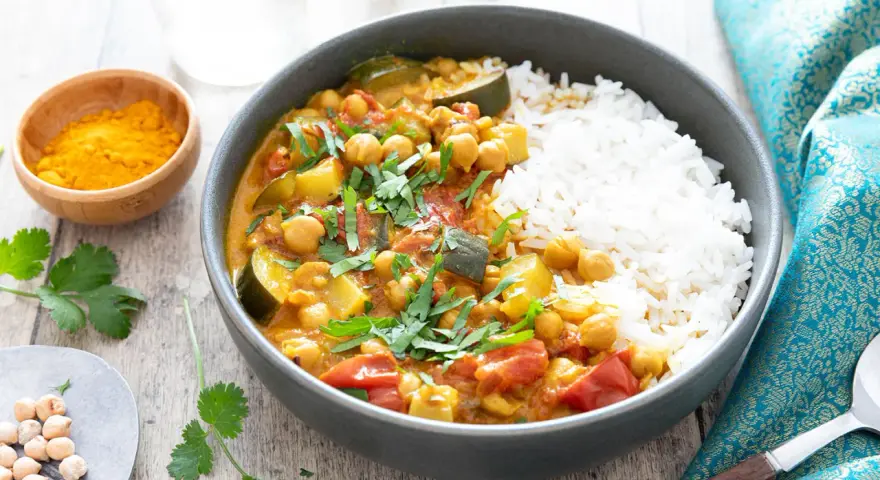 Un délicieux curry végétarien aux pois chiches, courgettes et tomates, servi avec du riz blanc et garni de coriandre fraîche.