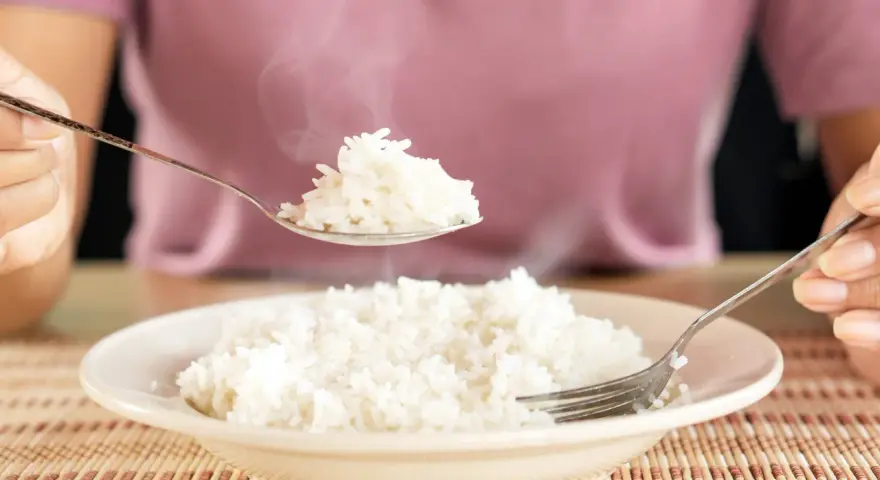 Une cuillère de riz blanc fumant, résultat d'une cuisson parfaite, est soulevée au-dessus d'une assiette remplie.