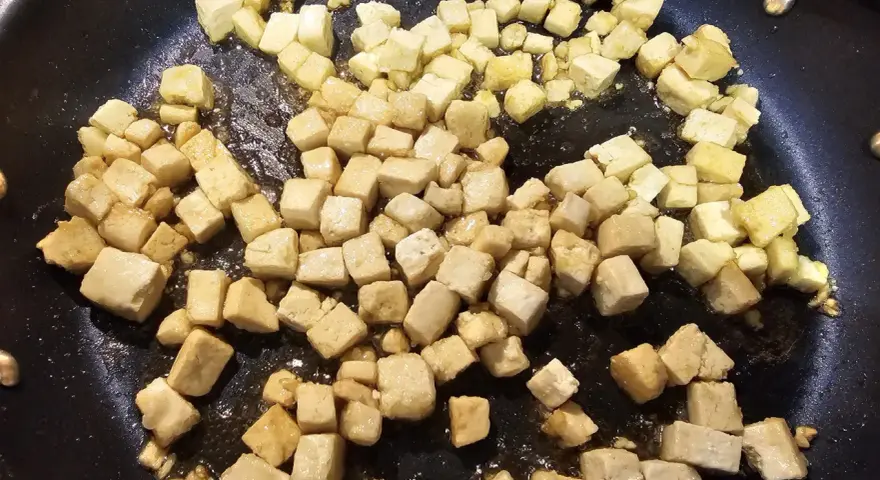 Dés cubes de tofu caramélisé dorent dans une poêle, prêts à être dégustés.