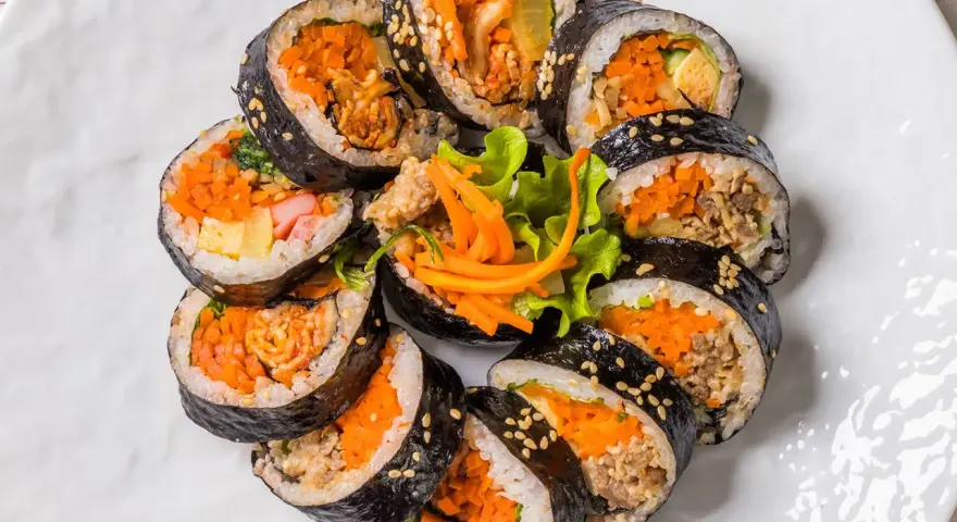 Un assortiment de makis végétariens colorés, garnis de carottes râpées, d'omelette et de légumes croquants, disposés en cercle sur une assiette blanche.