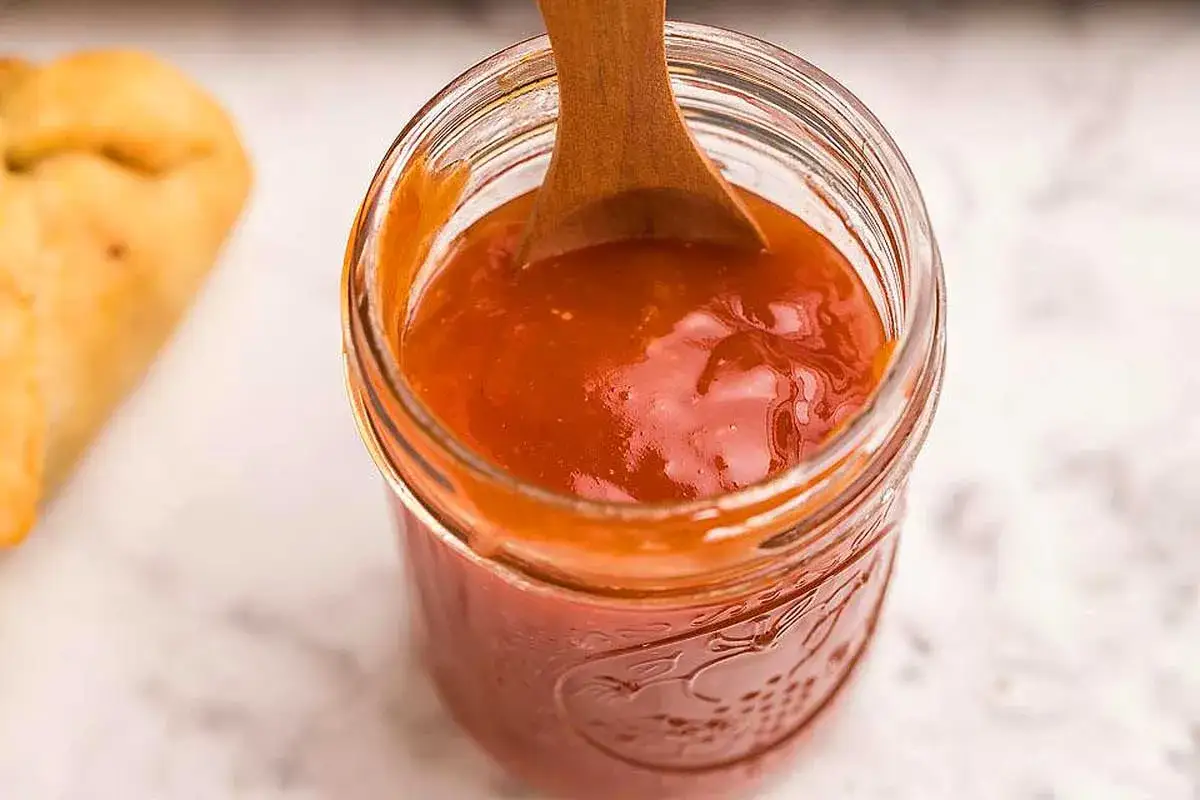 Cuillère en bois dans un pot de sauce sucré salé, prête à être dégustée avec un morceau de pain doré.