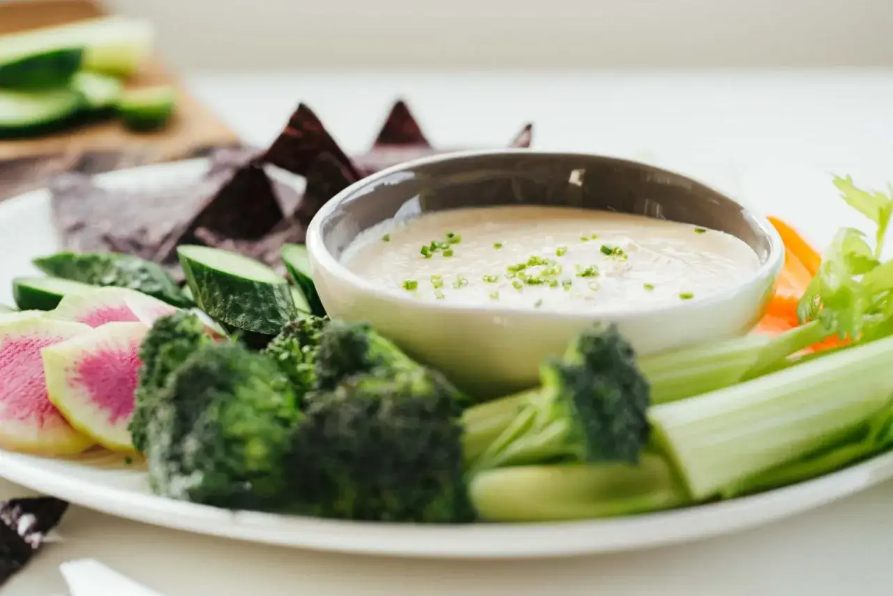 Assiette de crudités colorées avec un bol de sauce dip crémeuse, garnie de ciboule.
