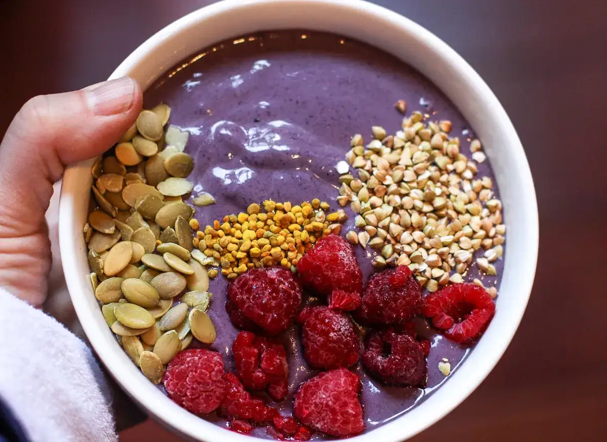 Bol de smoothie aux baies d'a&ccedil;a&iuml;, garni de framboises, de graines de citrouille, de pollen et de sarrasin.