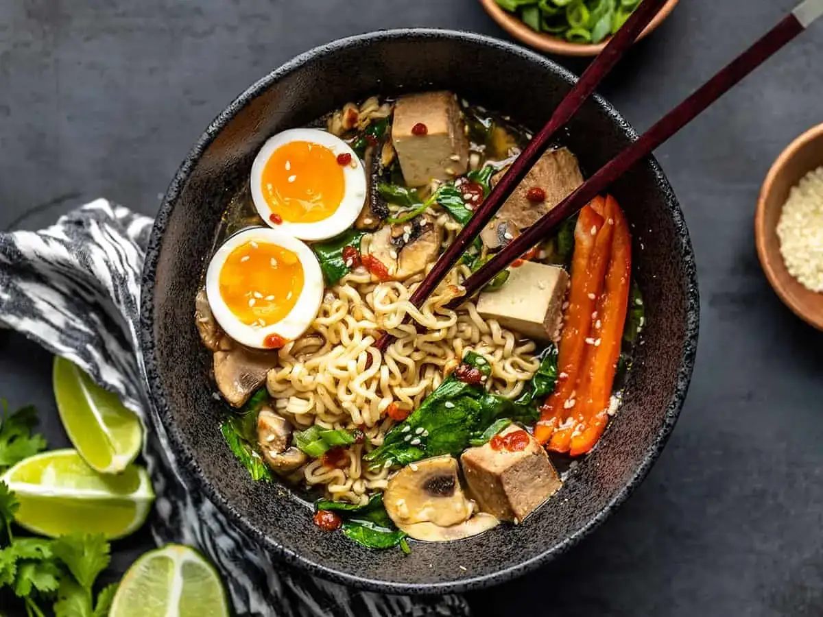 Un bol de pâtes ramen savoureux avec des œufs mollets, du tofu, des champignons et des poivrons.