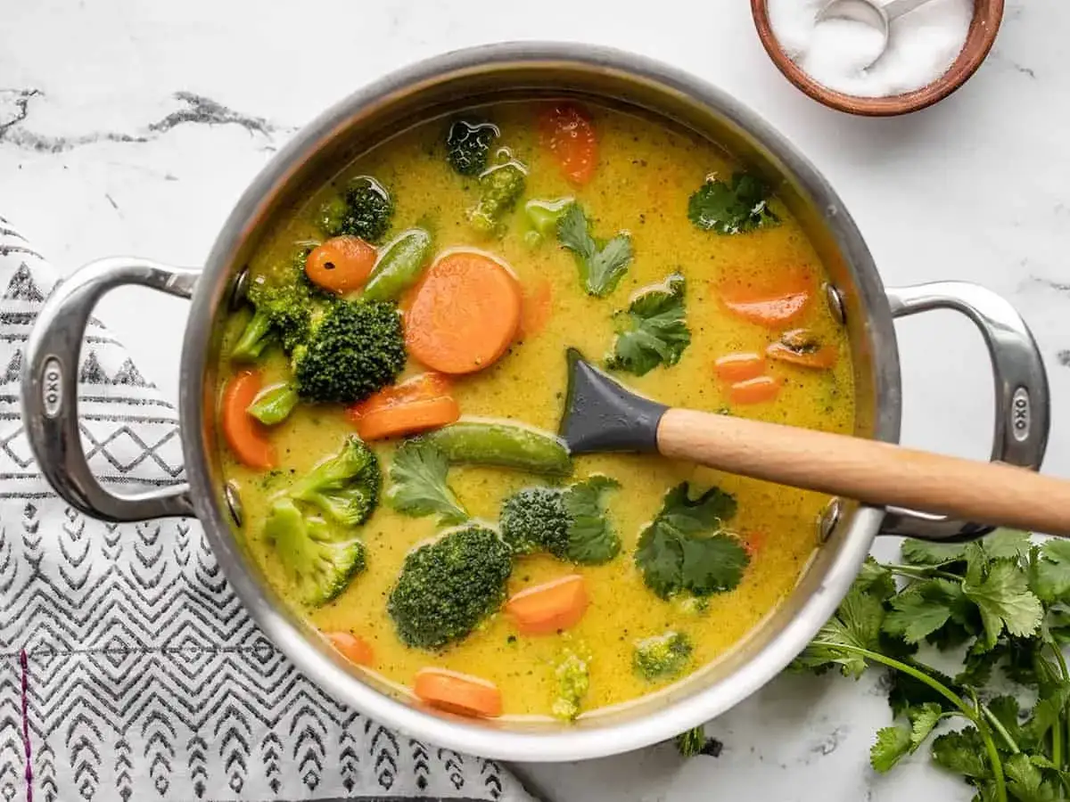 Un plat de curry végétarien mijote dans une casserole, avec du brocoli, des carottes et des pois mange-tout.