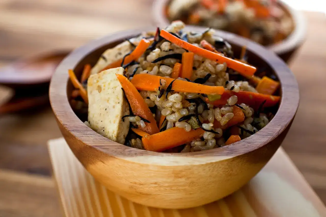 Un bol en bois rempli de riz germé, de carottes coupées en julienne et de tofu.