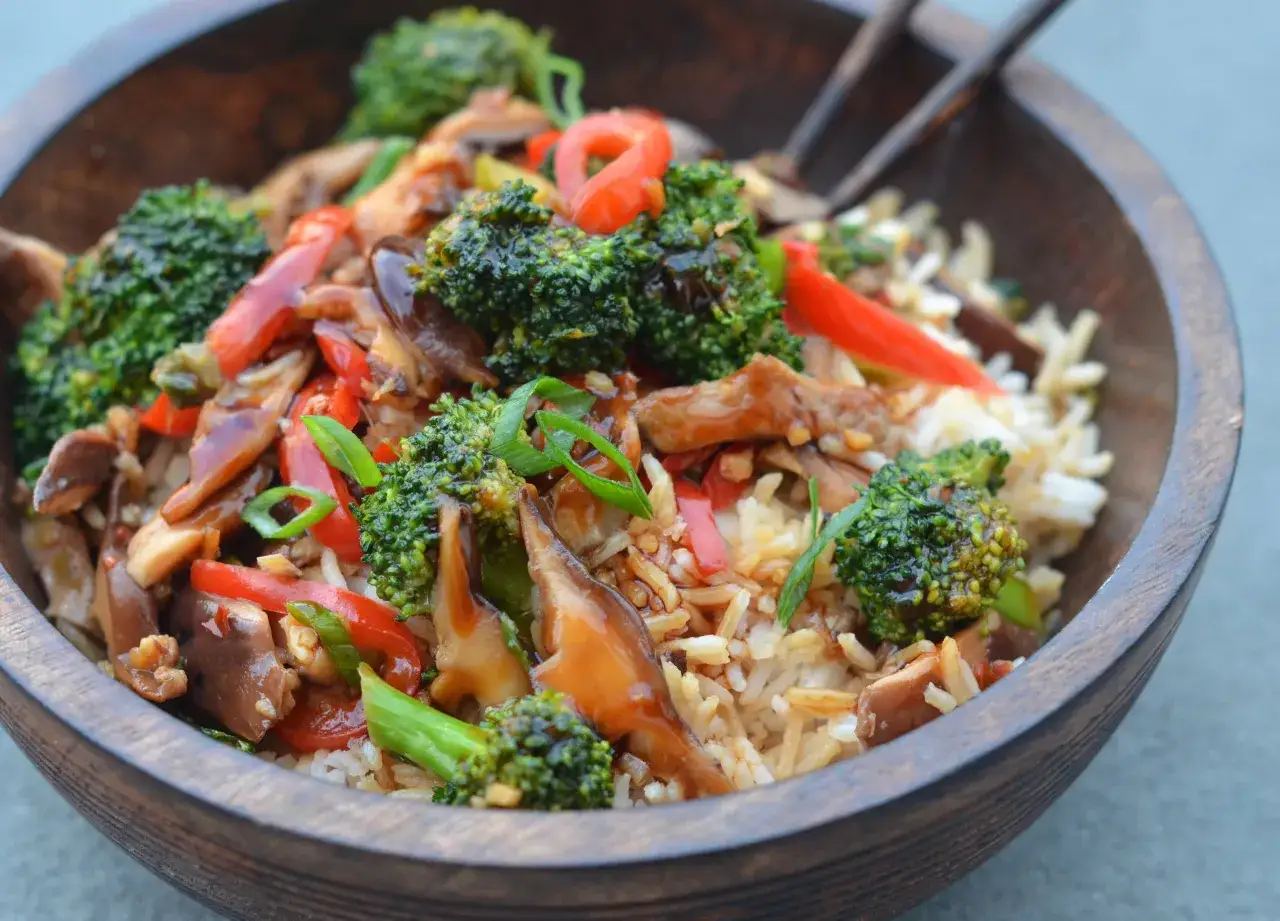 Un d&eacute;licieux wok de l&eacute;gumes asiatique avec du riz, du brocoli, des poivrons rouges et des champignons, garni de ciboule.
