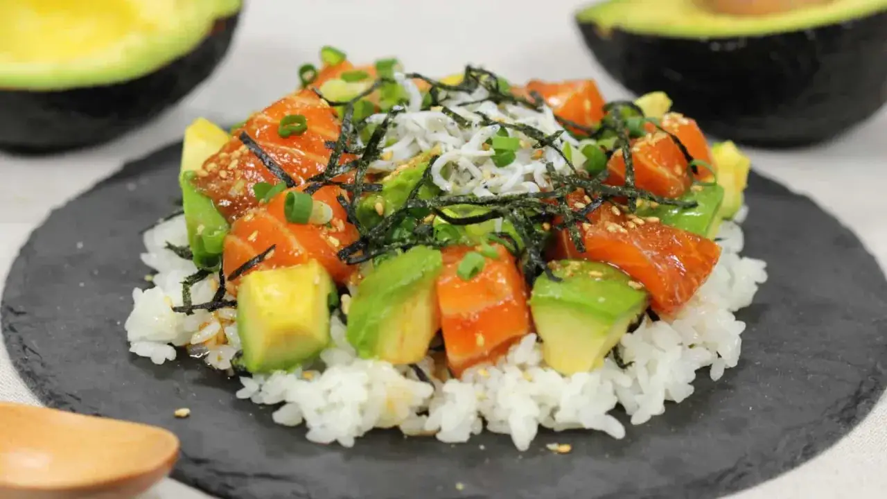 Un délicieux poke bowl riz avec saumon, avocat, et petites sardines, garni d'algues et de ciboule.