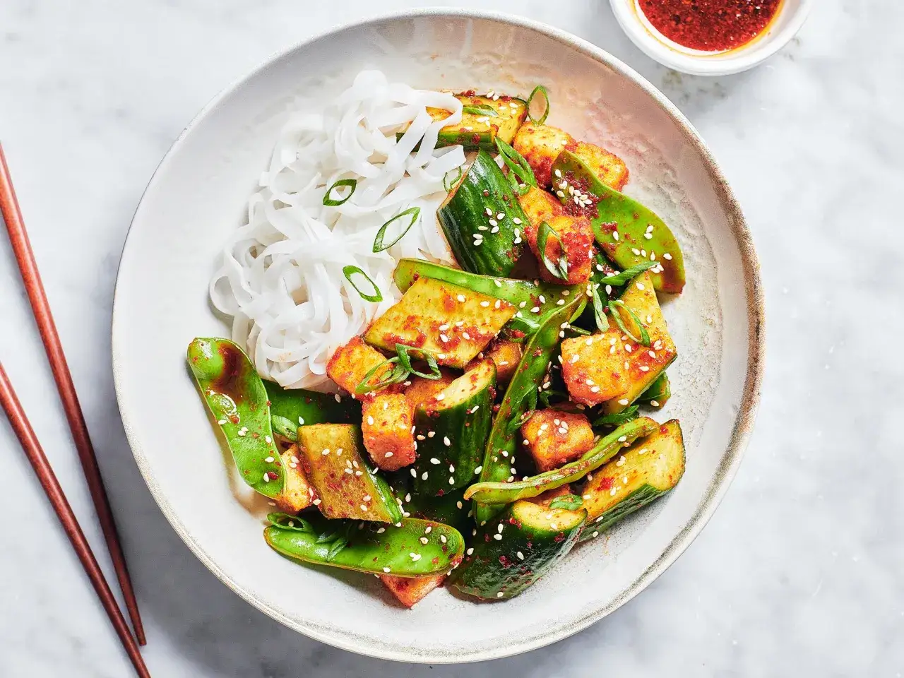 Un bol de nouilles de riz avec du bibimbap au tofu, des pois mange-tout et du concombre, garni de graines de s&eacute;same et d'oignons verts.