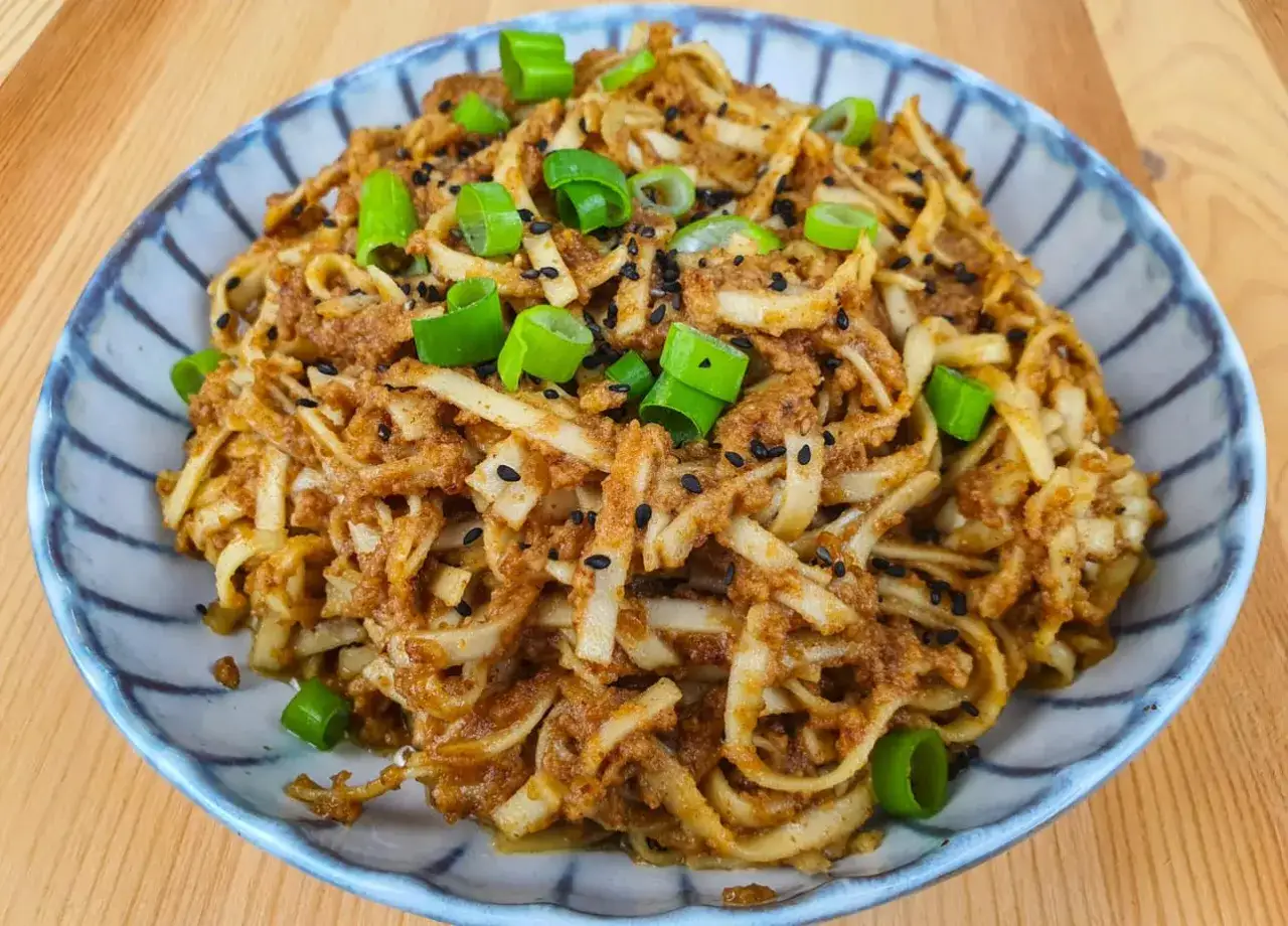 Un plat de p&acirc;tes cacahu&egrave;te, garni de ciboule fra&icirc;che et de graines de s&eacute;same noir, pr&ecirc;t &agrave; &ecirc;tre d&eacute;gust&eacute;.