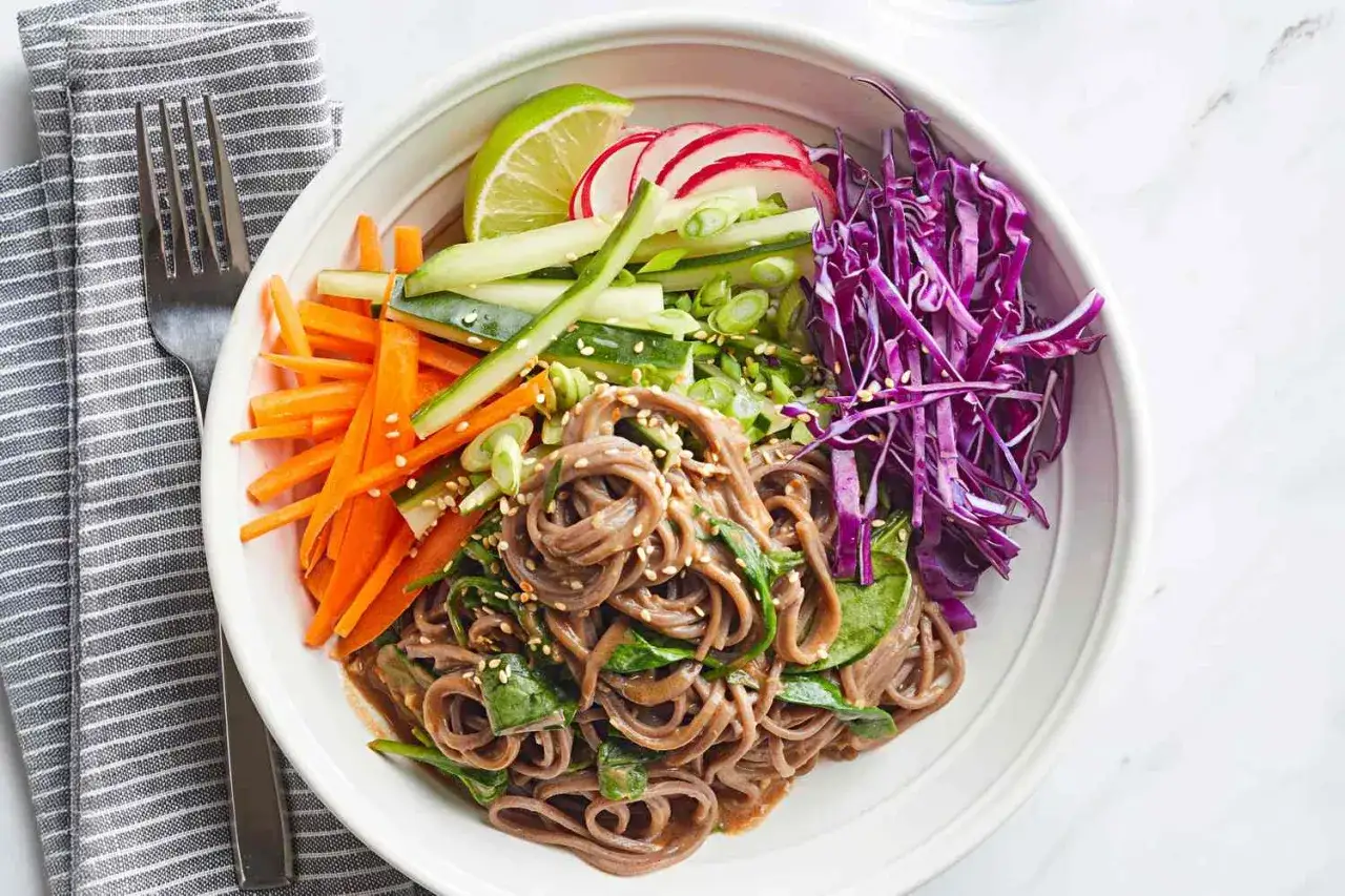 Un bol color&eacute; de nouilles soba garni de carottes r&acirc;p&eacute;es, concombre, radis, chou rouge et oignons verts.