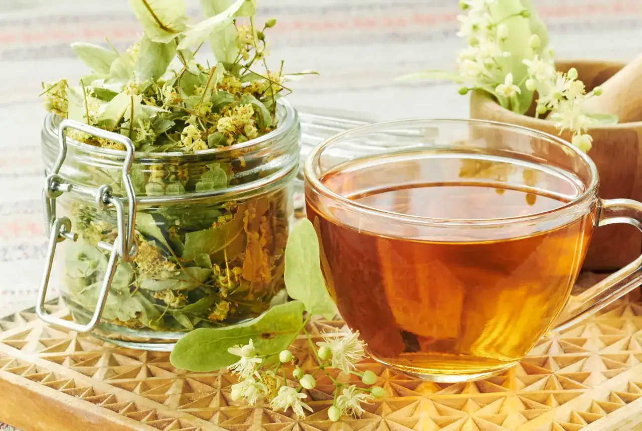 Tasse de th&eacute; ambr&eacute; &agrave; c&ocirc;t&eacute; d'un bocal de fleurs de tilleul s&eacute;ch&eacute;es, &eacute;voquant les bienfaits apaisants de cette infusion.