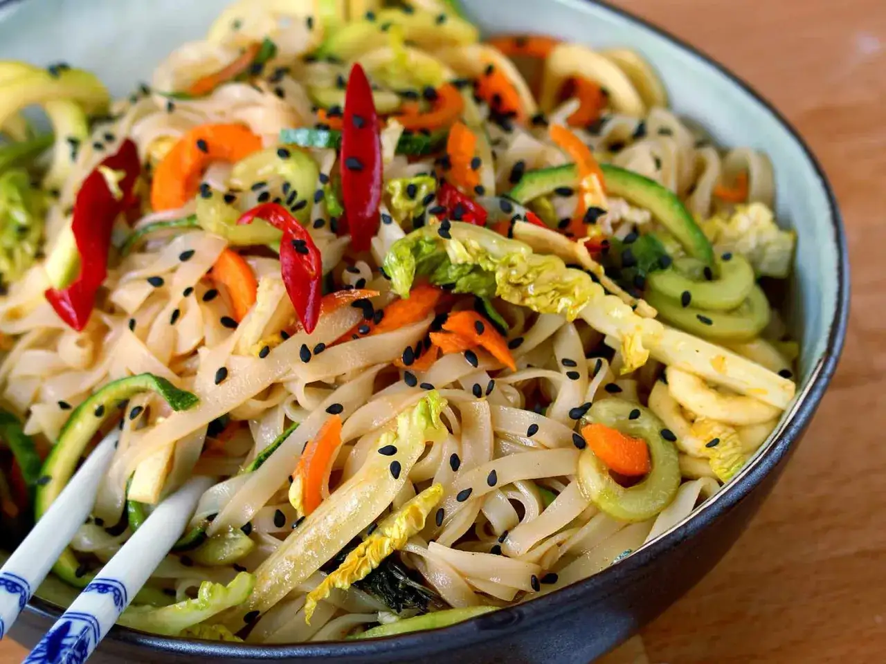 Un bol de salade de nouilles thaï colorée avec des piments rouges, des carottes, des courgettes et des graines de sésame noir.