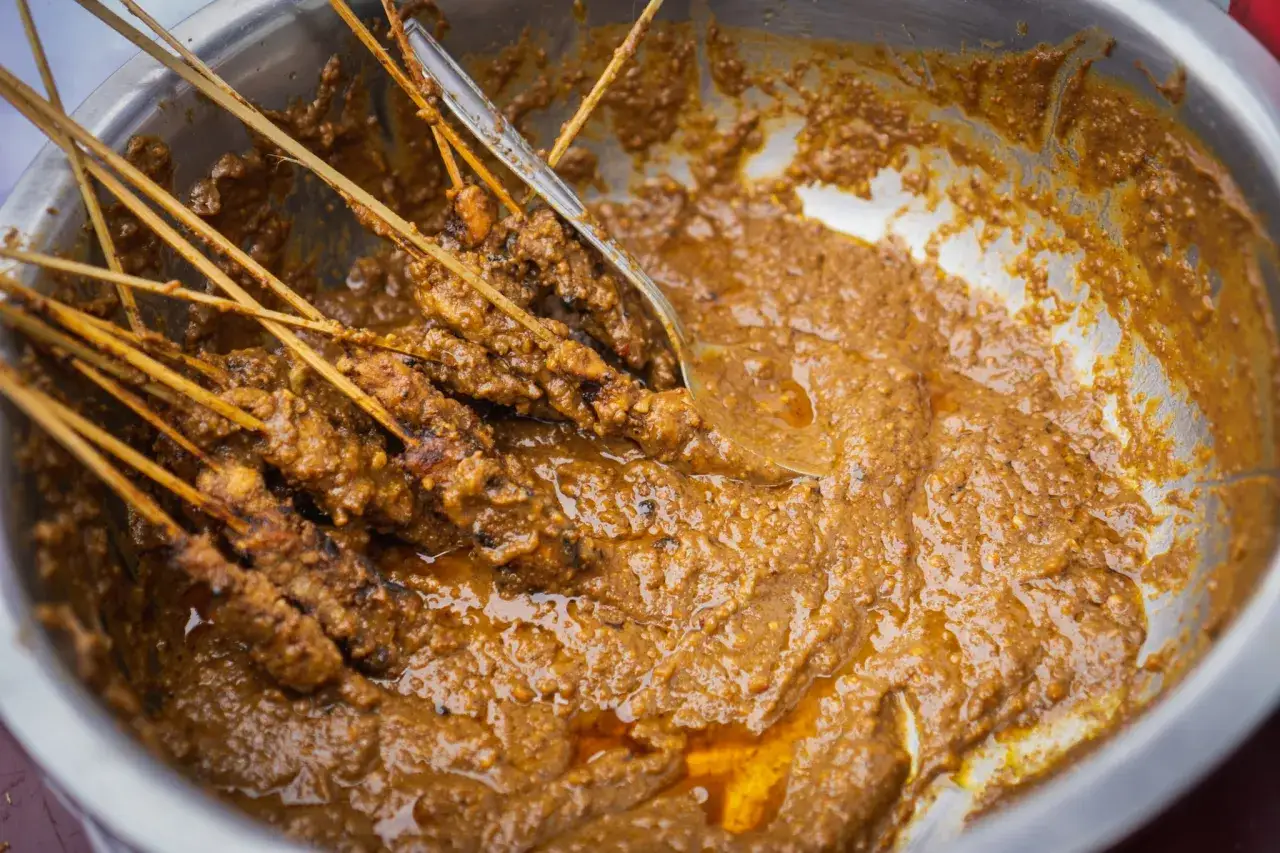 Brochettes de poulet baignant dans une sauce satay crémeuse et riche, prête à être dégustée.