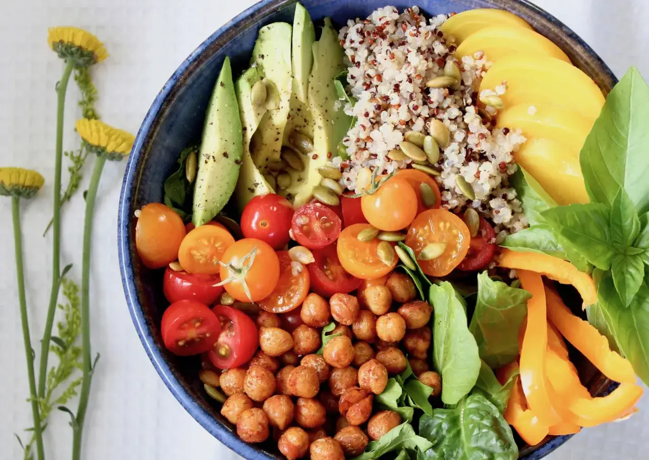Un délicieux bouddha bowl coloré avec quinoa, avocat, tomates cerises, pois chiches rôtis, poivron orange et basilic frais.