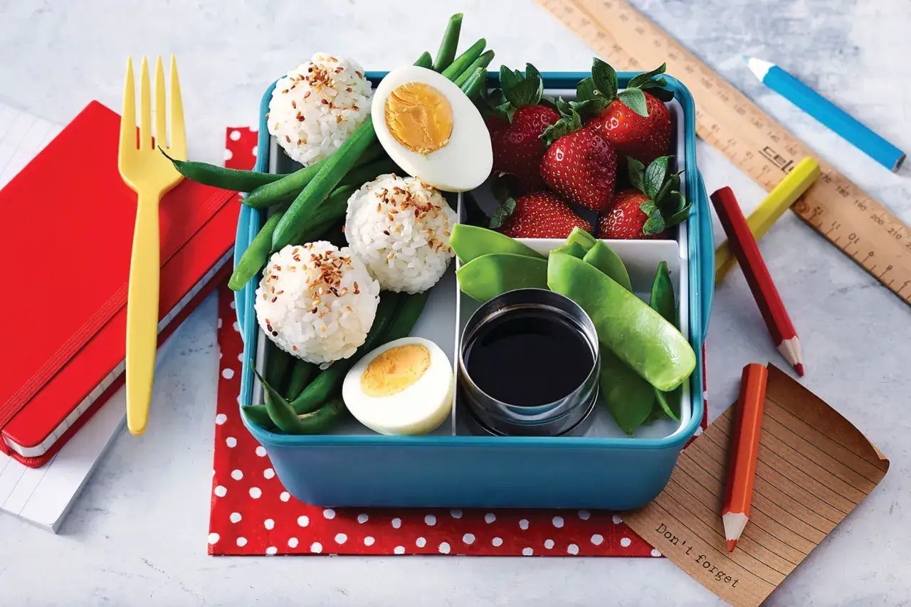 Bo&icirc;te &agrave; lunch avec des onigiri, des haricots verts, des fraises, des &oelig;ufs durs et une sauce soja. Parfait pour un pique-nique ou un d&eacute;jeuner sur le pouce.