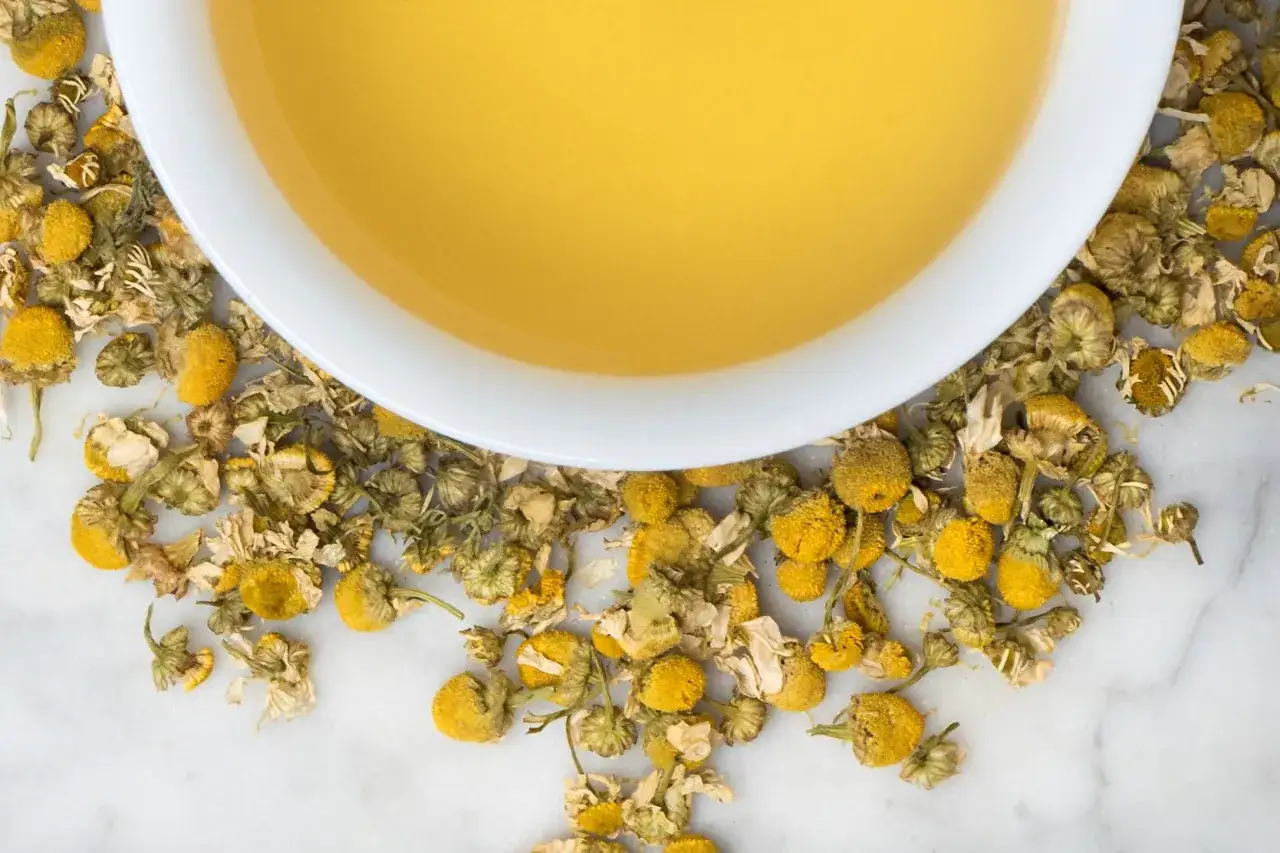 Infusion dorée de camomille, entourée de fleurs séchées. Un remède naturel pour ses bienfaits apaisants.
