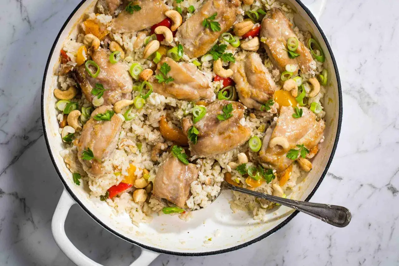 Un plat de poulet et riz coco, garni de noix de cajou, oignons verts et persil. Une recette savoureuse et color&eacute;e.