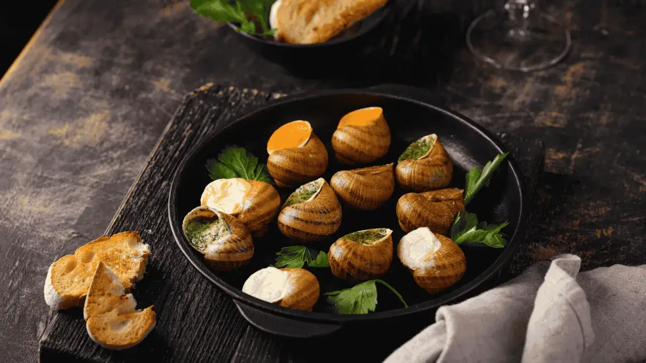 Plat d'escargots dans une poêle, avec du pain grillé. Attention, une allergie escargot peut survenir.