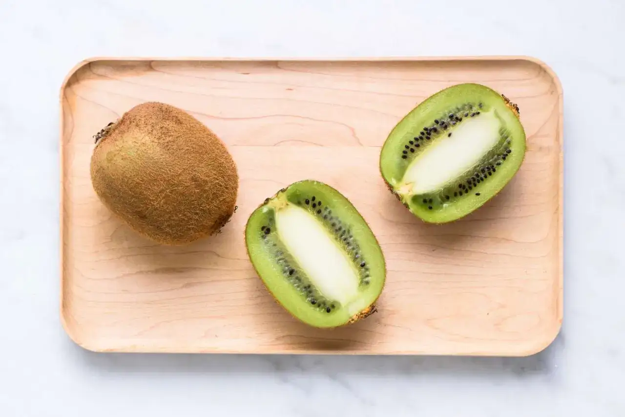Un kiwi entier et deux moiti&eacute;s sur un plateau en bois. Attention, ce kiwi langue qui pique peut surprendre !