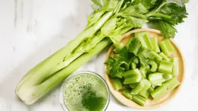 Jus de céleri frais, coupé en morceaux dans un bol en bois. Une branche entière de céleri est à côté. Attention à l'allergie céleri.