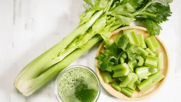 Jus de céleri frais, coupé en morceaux dans un bol en bois. Une branche entière de céleri est à côté. Attention à l'allergie céleri.